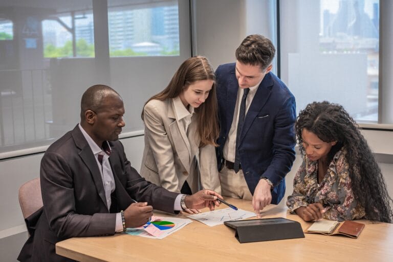 Four professionals collaborating around a table to analyze charts and documents as part of an IT audit.