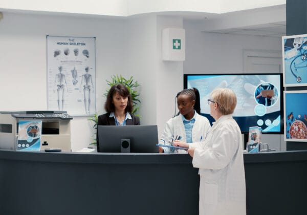Three healthcare professionals discussing in front of a computer workstation to optimize the management of electronic health records.